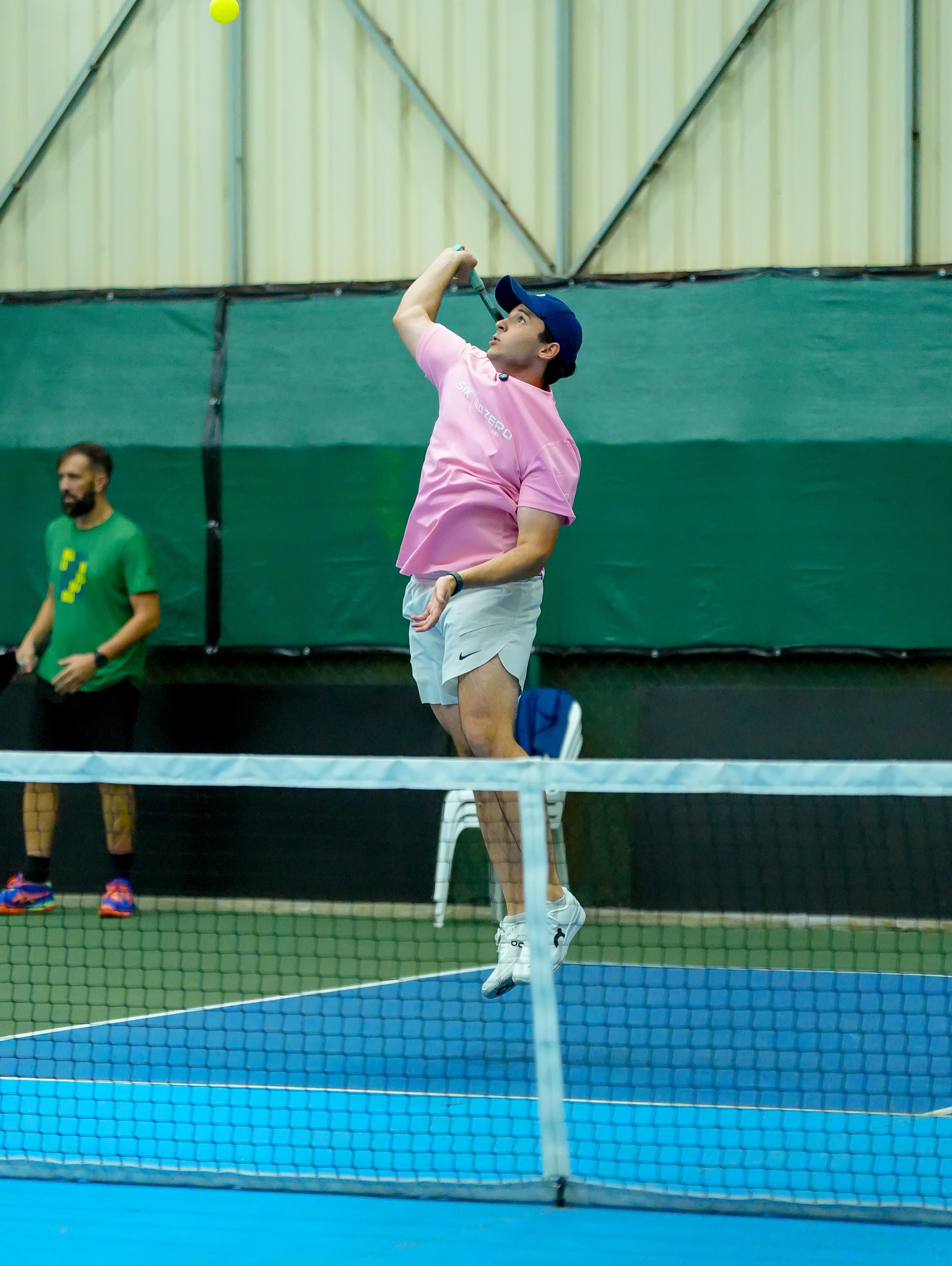 Atleta de camiseta rosa no alto, raquete acima da cabeça