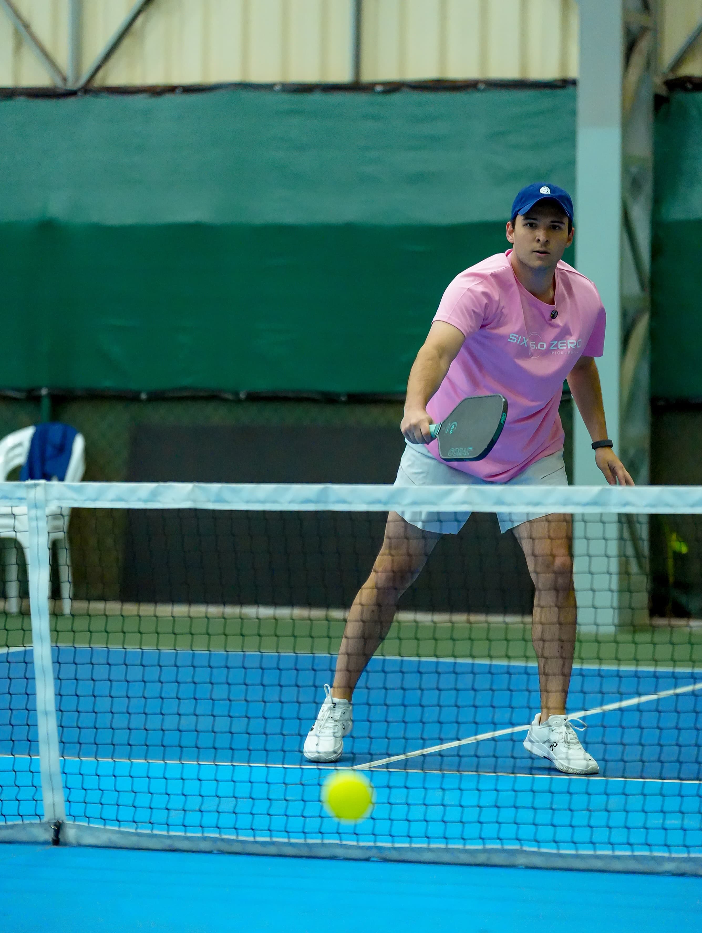 Atleta de camiseta rosa junto à rede, bola quicando na quadra