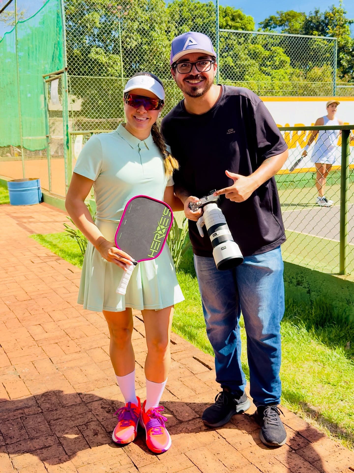 Arruda com a câmera e a teleobjetiva ao lado da atleta Marcela Donatoni, com raquete de pickleball